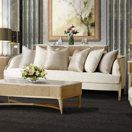 Luxury living room featuring a cream upholstered sofa with decorative throw pillows, a modern wood coffee table, floral centerpiece, abstract wall art, elegant table lamps, and a neutral contemporary interior design.