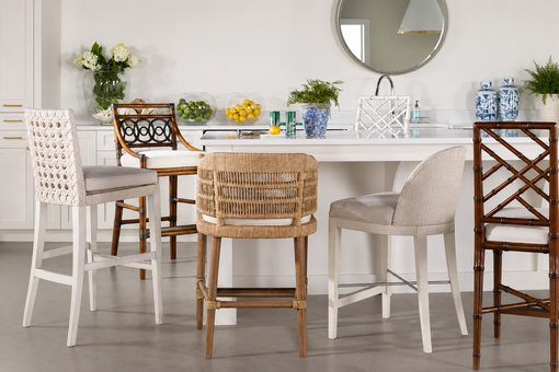 Modern kitchen island with five designer counter stools in woven, upholstered, and bamboo styles, featuring a white countertop, decorative plants, blue ceramic vases, and contemporary coastal-inspired décor.