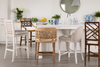 Modern kitchen island with five designer counter stools in woven, upholstered, and bamboo styles, featuring a white countertop, decorative plants, blue ceramic vases, and contemporary coastal-inspired décor.