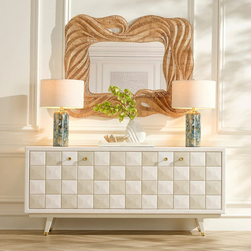 Modern white sideboard with geometric drawer fronts, paired with blue ceramic table lamps, a woven rattan wall mirror, and decorative greenery in a bright luxury living room.