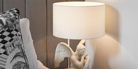 Decorative lamp with a gargoyle design on a bedside table next to a bed with patterned headboard and pillows.