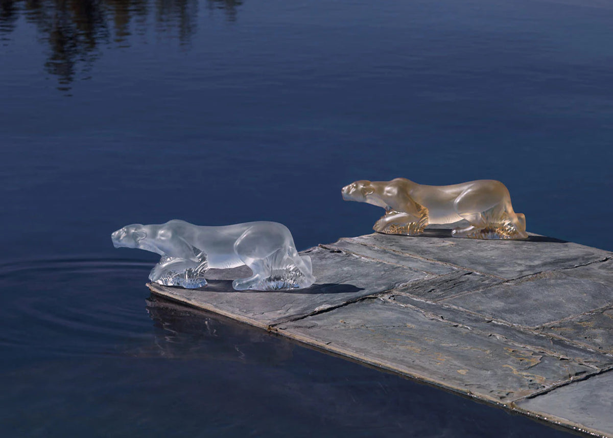 Two glass polar bear sculptures on a stone platform over water 