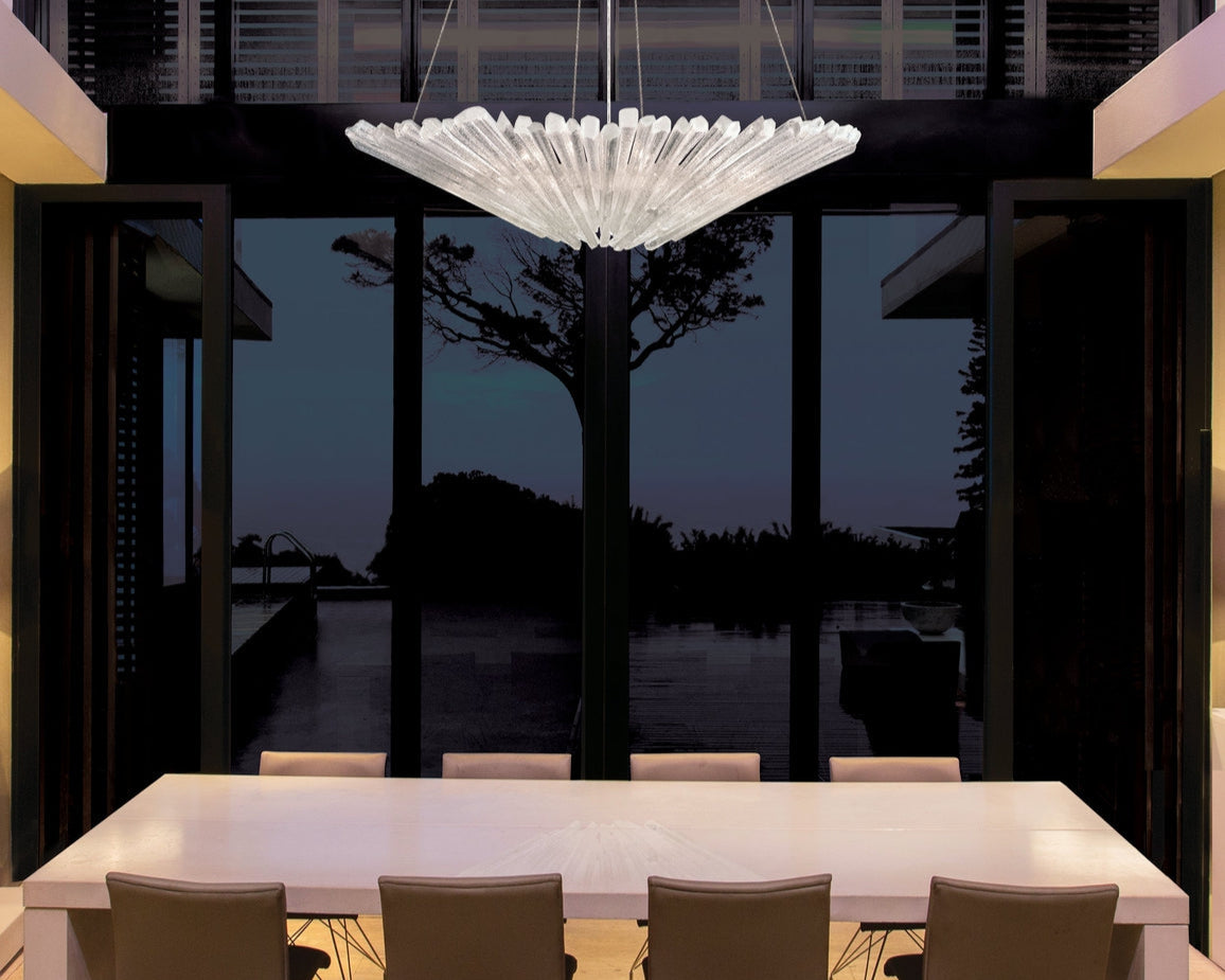 Modern dining area with a large chandelier and a view of water at night.