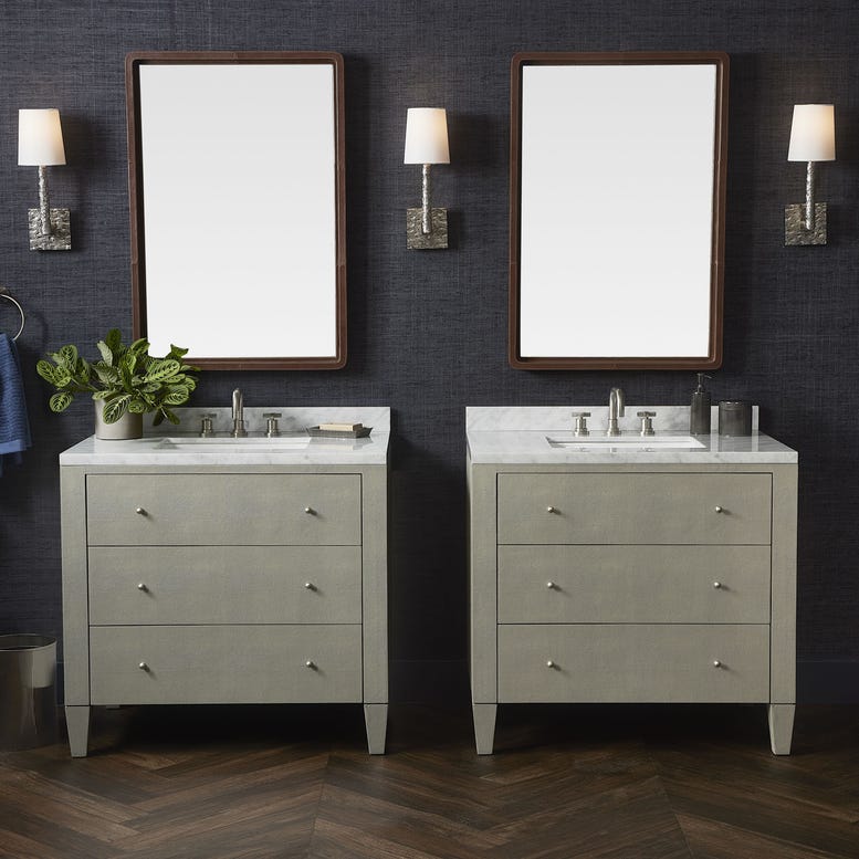 A stylish bathroom featuring two matching vanities with marble tops, framed mirrors, wall sconces, and a potted plant.