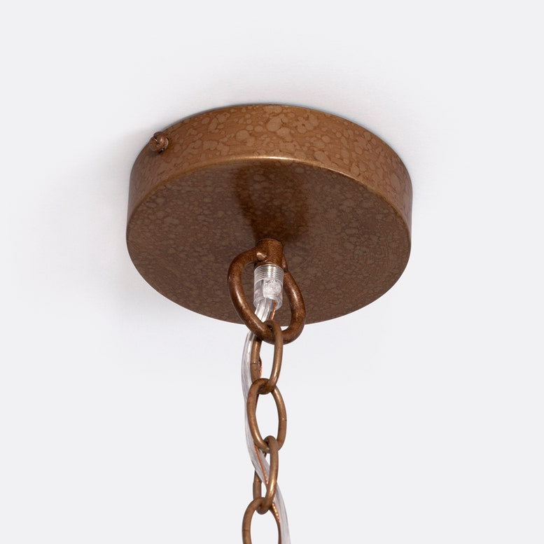 A close-up view of a textured bronze Magdalena Rattan Pendantt with a metal chain and transparent wiring, suspended against a light background.