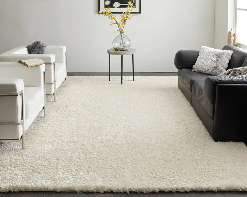 Living room with a large white rug, black sofa, and white chairs.