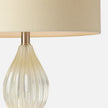 A close-up of an elegant lamp featuring a ribbed glass base and a soft beige fabric shade, highlighting its modern design.